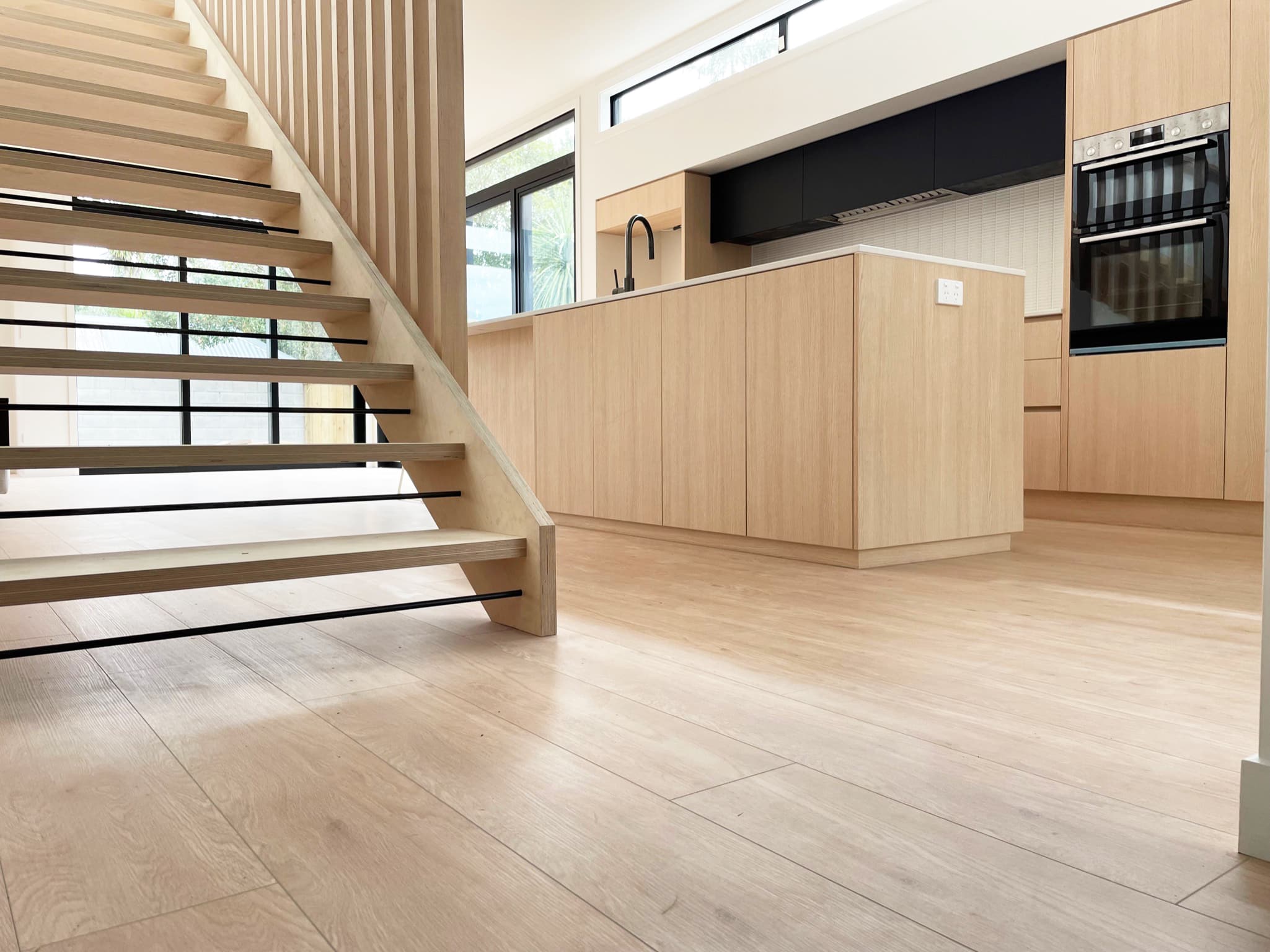 An oiled oak floor running through a hallway to a kitchen, with an open stair.